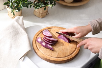 Photo of Woman cutting red onion into slices at countertop in kitchen, closeup