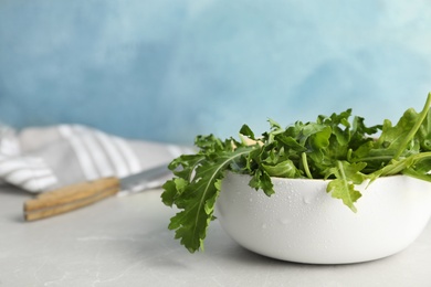 Photo of Fresh arugula in bowl on light grey table. Space for text