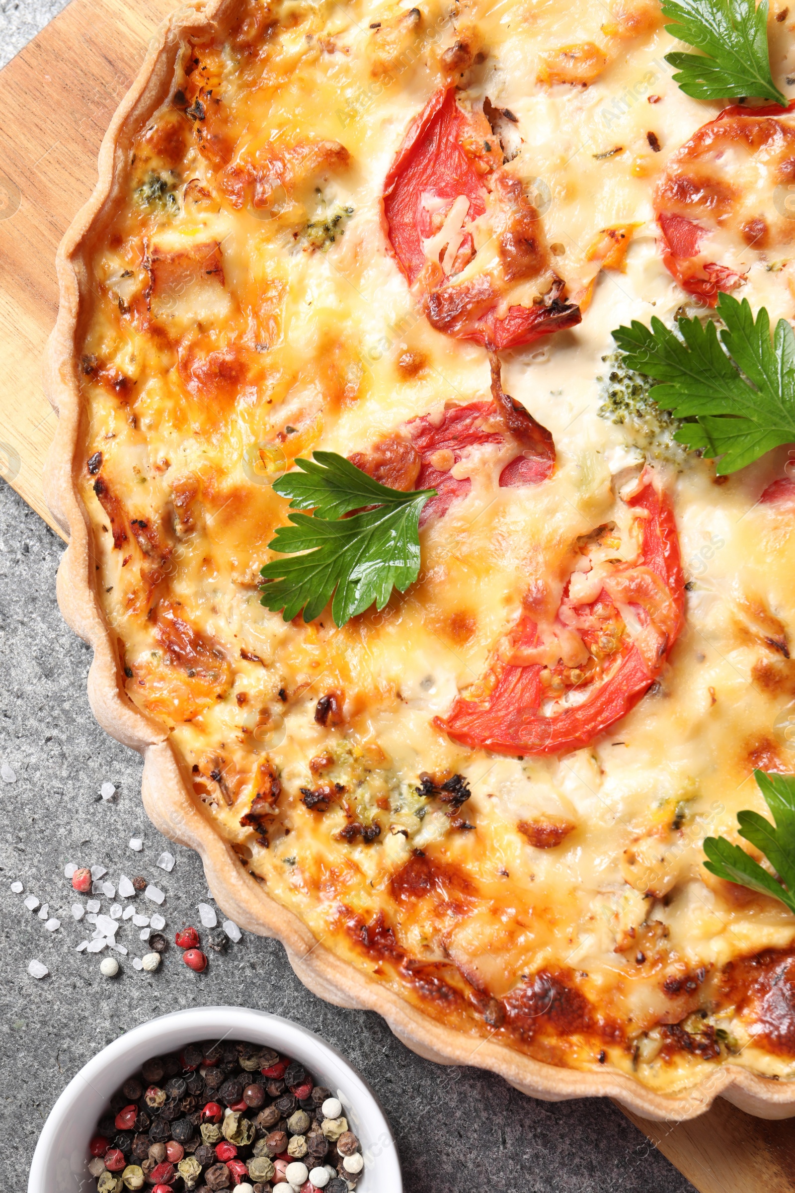 Photo of Tasty quiche with tomatoes, parsley and cheese served on grey textured table, flat lay