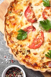 Tasty quiche with tomatoes, parsley and cheese served on grey textured table, flat lay