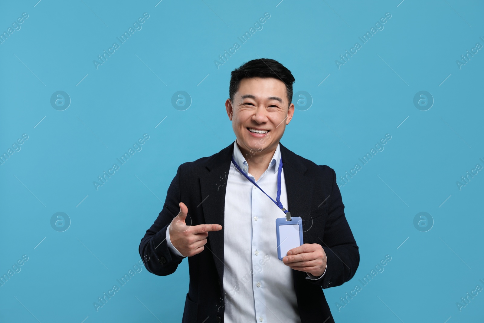 Photo of Happy asian man pointing at vip pass badge on light blue background