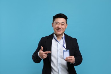 Photo of Happy asian man pointing at vip pass badge on light blue background
