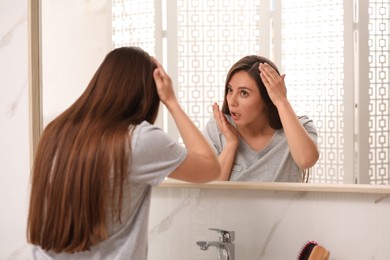 Emotional woman with hair loss problem looking in mirror indoors