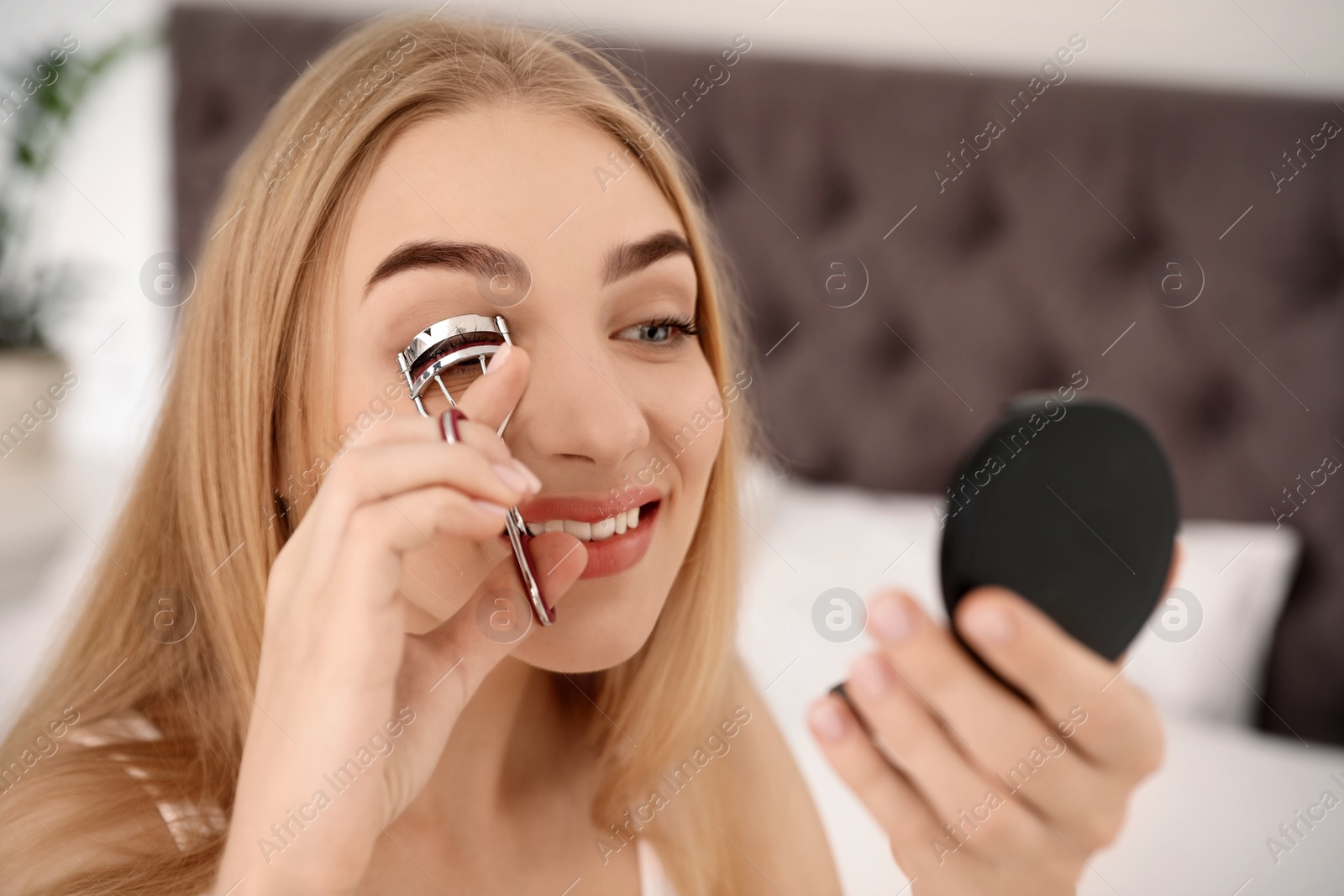 Photo of Young woman curling her eyelashes at home