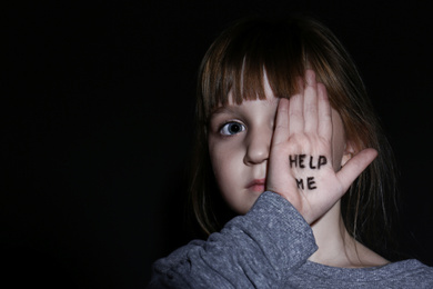 Photo of Abused little girl showing palm with phrase HELP ME on black background, space for text. Domestic violence concept