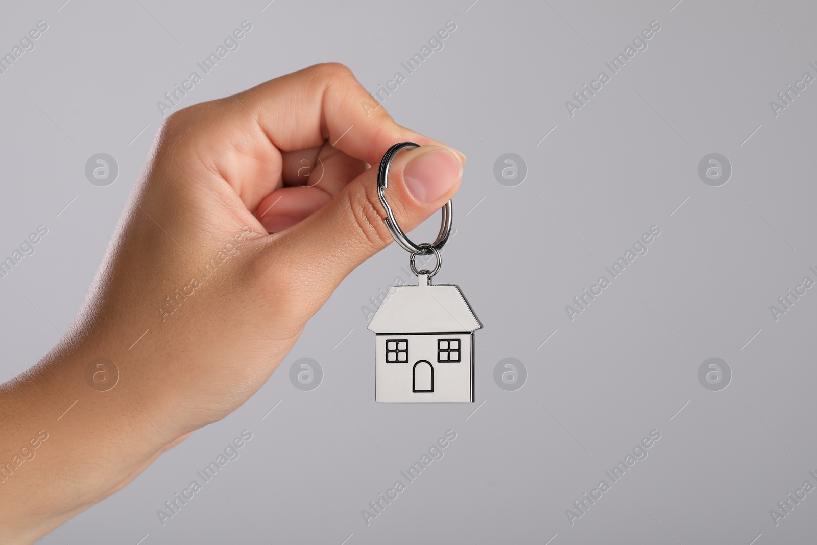 Photo of Woman holding metallic keychain in shape of house on grey background, closeup. Space for text