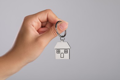 Woman holding metallic keychain in shape of house on grey background, closeup. Space for text