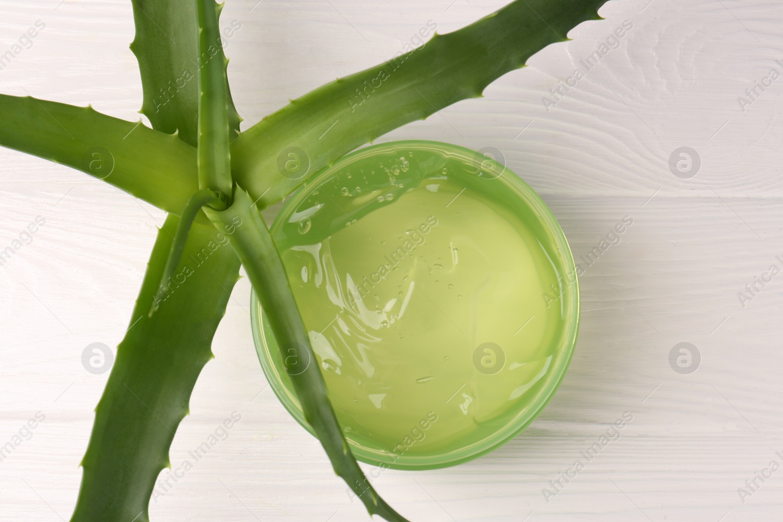 Photo of Jar of cosmetic gel and aloe vera leaves on white wooden table, top view