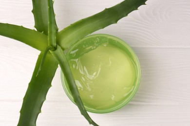 Photo of Jar of cosmetic gel and aloe vera leaves on white wooden table, top view
