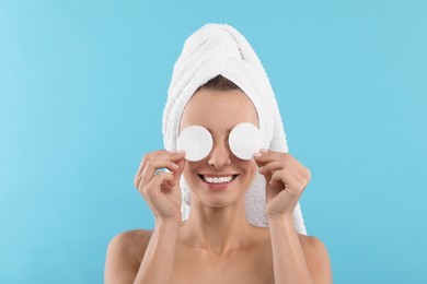 Photo of Smiling woman removing makeup with cotton pads on light blue background