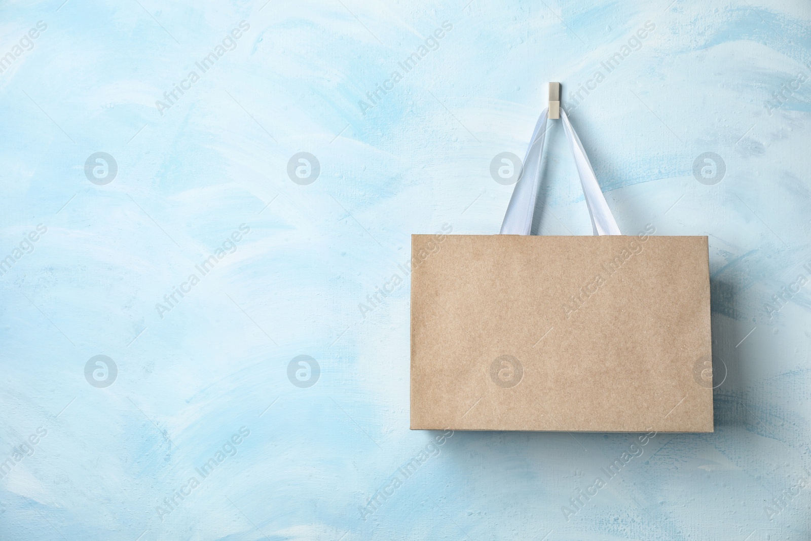 Photo of Paper shopping bag with ribbon handles hanging on color wall. Mockup for design