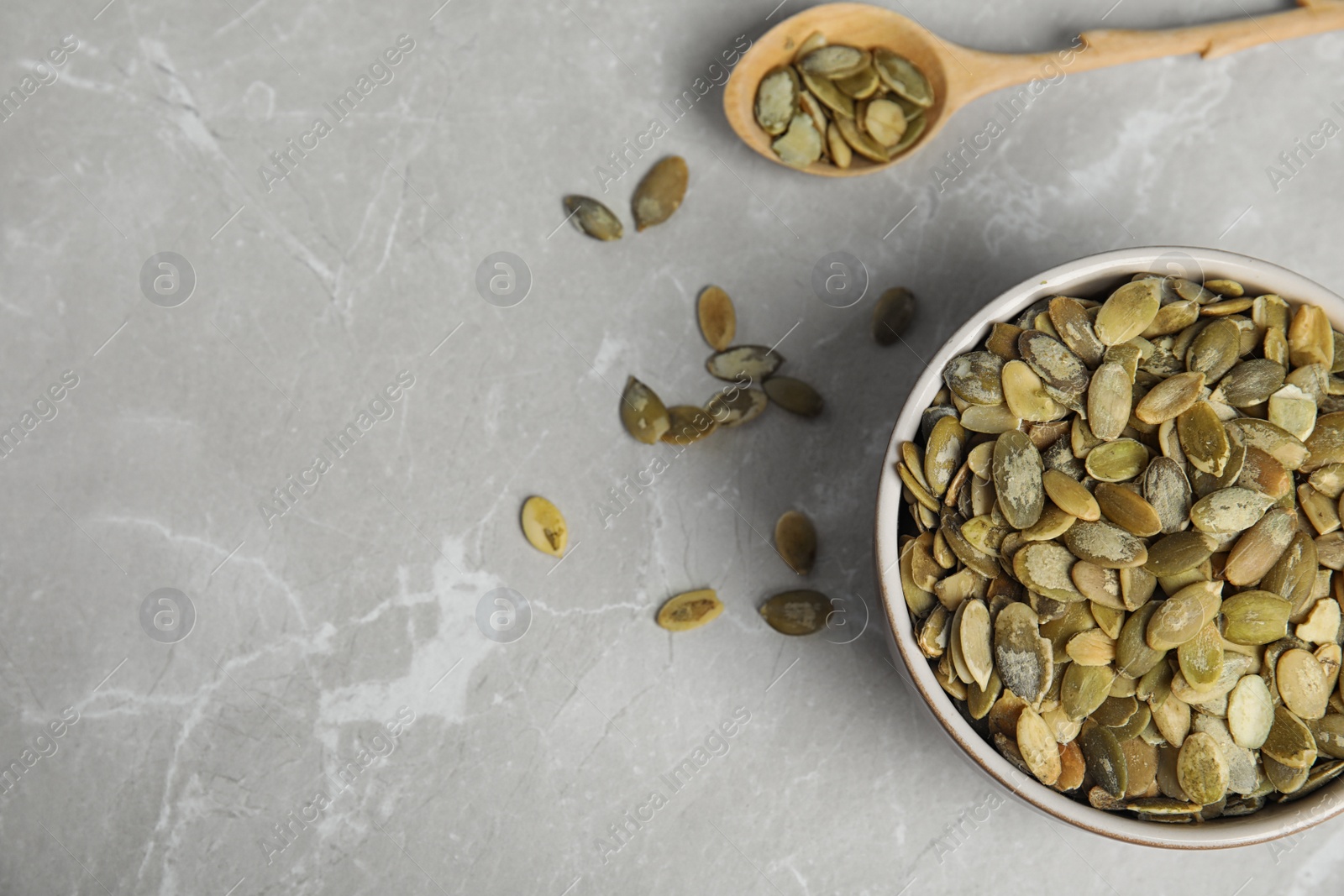 Photo of Bowl of raw pumpkin seeds on light grey marble table, flat lay. Space for text