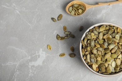 Photo of Bowl of raw pumpkin seeds on light grey marble table, flat lay. Space for text