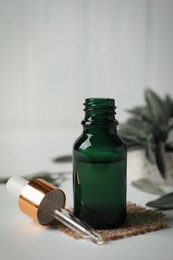 Bottle of essential sage oil, dropper and leaves on white table