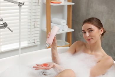 Woman pouring shower gel onto hand in bath indoors