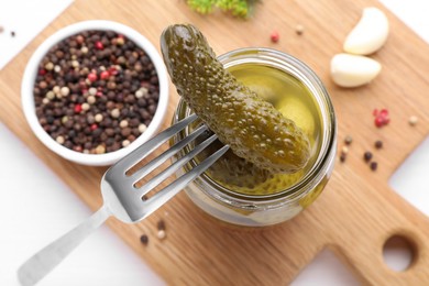 Photo of Fork with tasty pickled cucumber near jar on table, above view