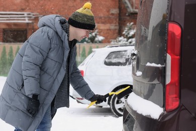 Man cleaning snow from car with brush outdoors