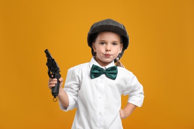 Cute little detective with revolver on yellow background