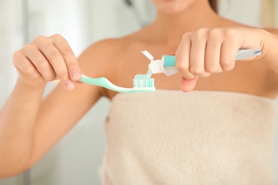 Woman applying toothpaste on brush indoors, closeup