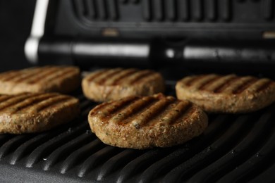 Delicious vegan cutlets cooking on electric grill, closeup