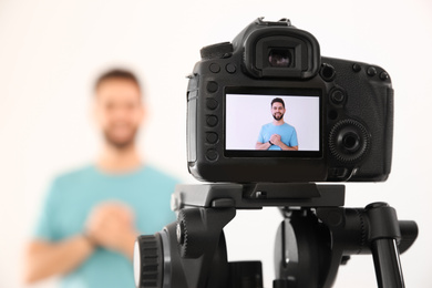 Young blogger shooting video with camera against white background, focus on screen