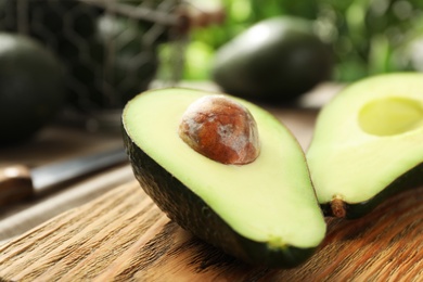 Halves of delicious ripe avocado on wooden board against blurred background