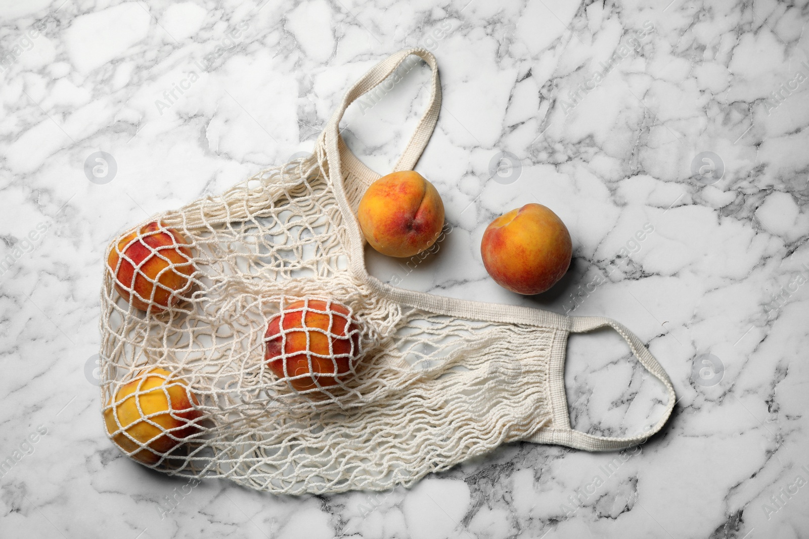 Photo of Net bag with fresh ripe peaches on white marble table, flat lay