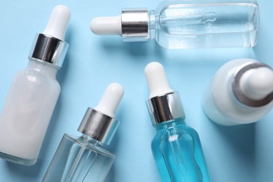 Many different bottles of cosmetic serum on light blue background, flat lay