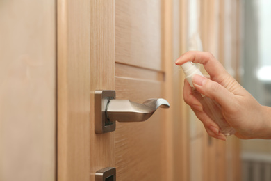 Woman spraying antiseptic onto door handle indoors, closeup