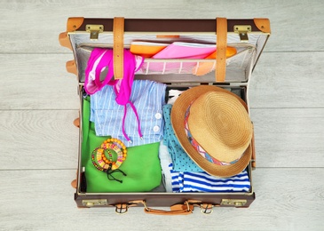 Photo of Open suitcase with different clothes and accessories packed for summer journey on floor