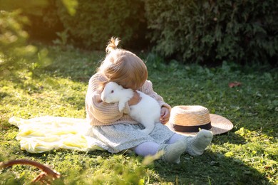 Photo of Cute little girl hugging adorable rabbit on green grass outdoors