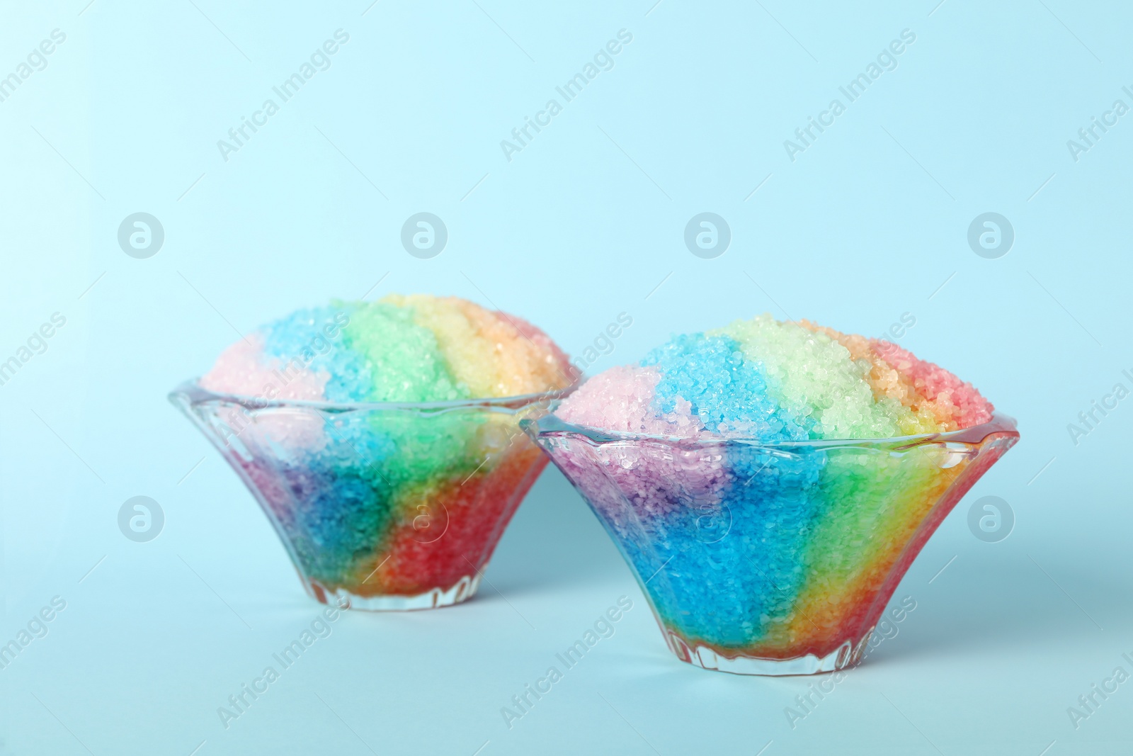 Photo of Rainbow shaving ice in glass dessert bowls on light blue background