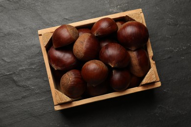 Roasted edible sweet chestnuts in wooden crate on grey textured table, top view
