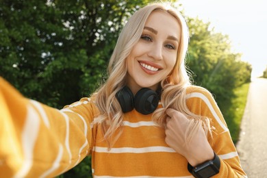 Smiling woman with headphones taking selfie in park on spring day