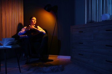 Photo of Confident young woman sitting under lamp light in cozy room at night