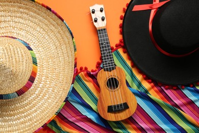 Mexican sombrero hats, guitar and colorful poncho on orange background, flat lay