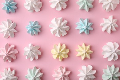 Many tasty meringue cookies on pink background, flat lay