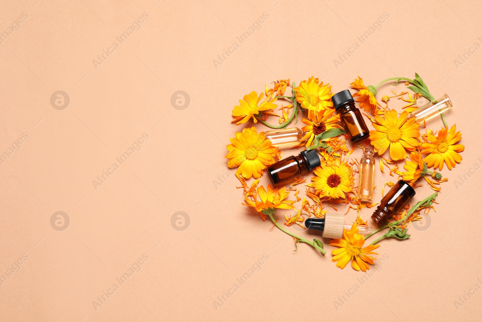 Photo of Heart made of bottles with essential oils and beautiful calendula flowers on beige background, flat lay. Space for text