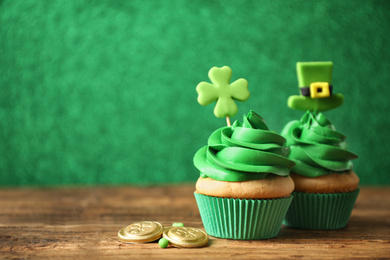 Photo of Decorated cupcakes and coins on wooden table, space for text. St. Patrick's Day celebration