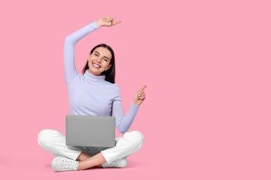 Photo of Happy woman with laptop pointing at something on pink background, space for text