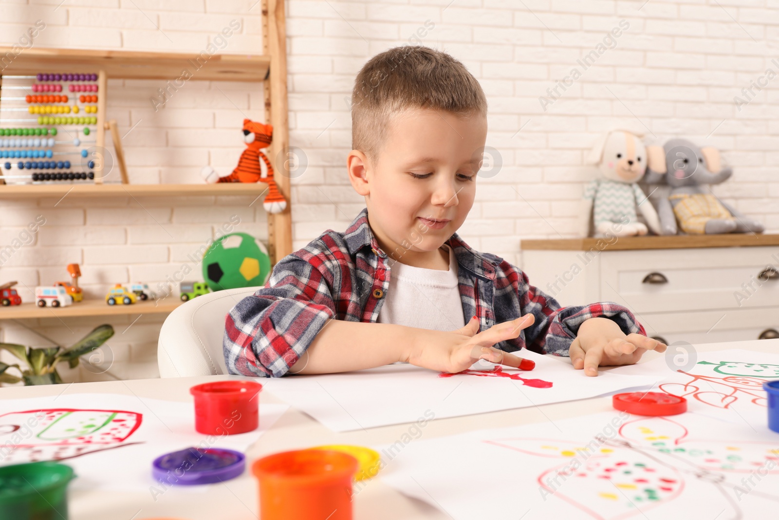 Photo of Little boy painting with finger at white table indoors