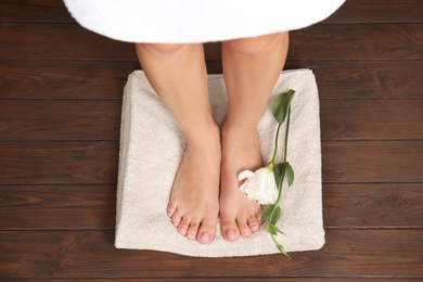 Photo of Woman with smooth feet, flower and towel standing on wooden floor, top view. Spa treatment