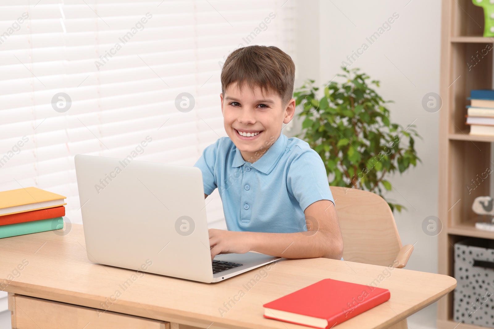 Photo of Smiling boy using laptop at desk in room. Home workplace