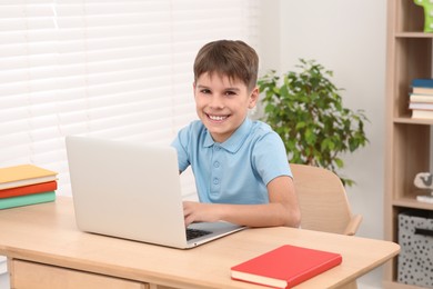 Smiling boy using laptop at desk in room. Home workplace