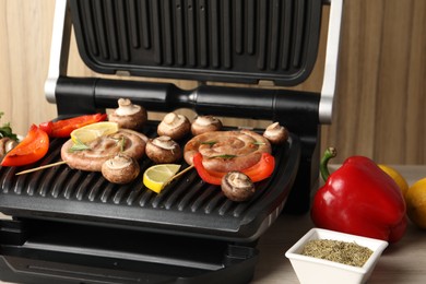 Electric grill with homemade sausages, vegetables and spices on wooden table