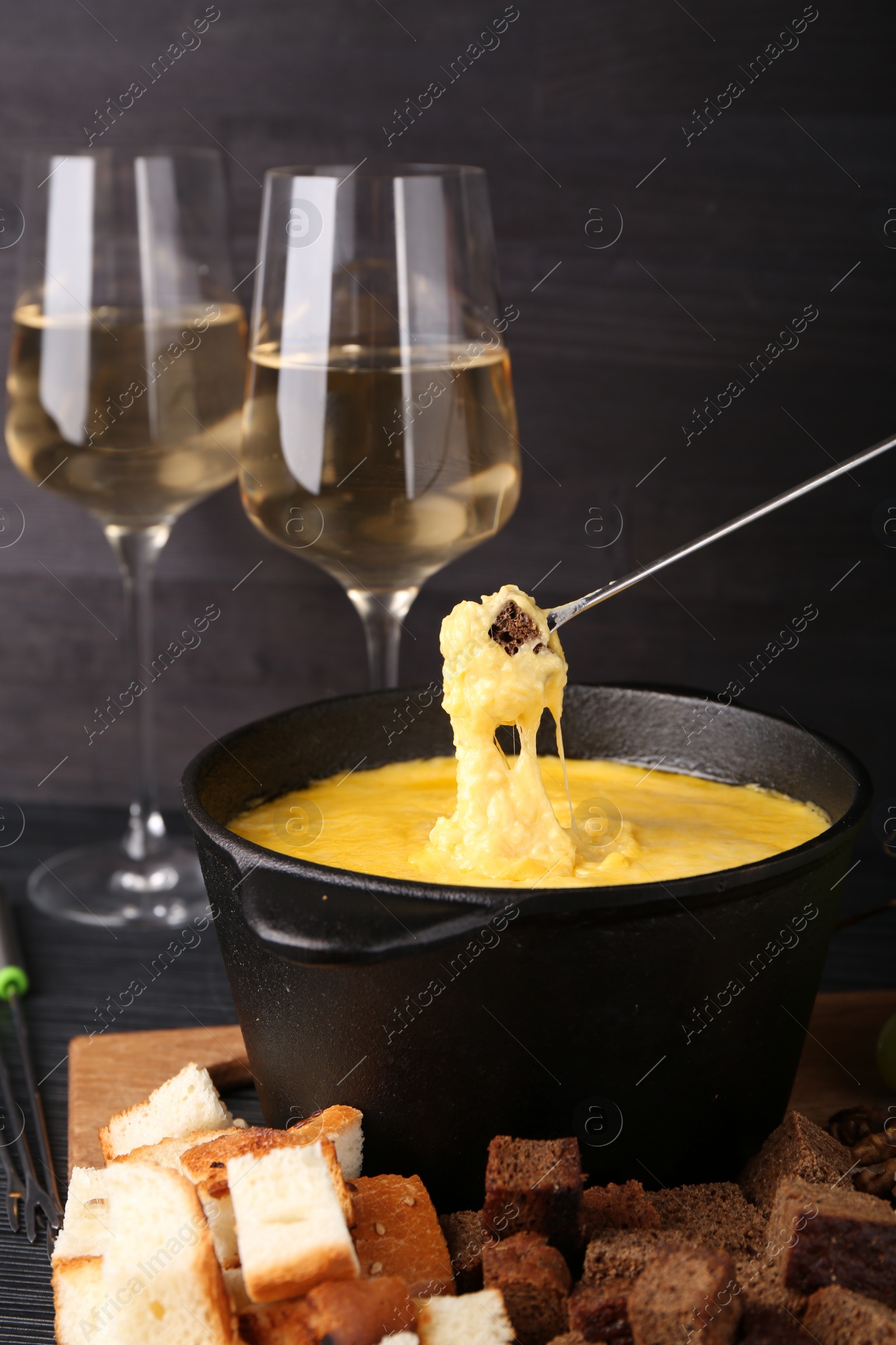 Photo of Dipping piece of bread into fondue pot with melted cheese on table