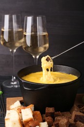 Photo of Dipping piece of bread into fondue pot with melted cheese on table