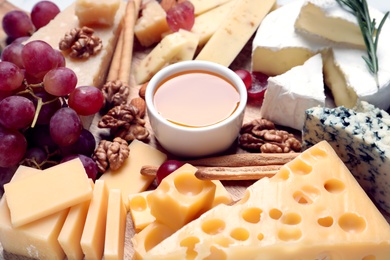 Photo of Cheese plate with honey, grapes and nuts on board, closeup