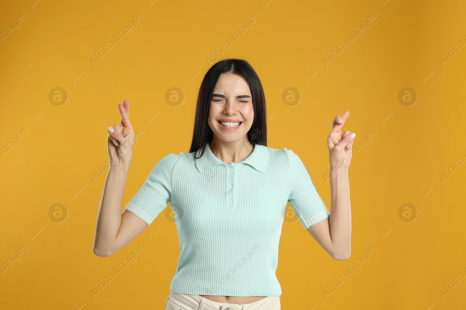 Photo of Woman with crossed fingers on yellow background. Superstition concept