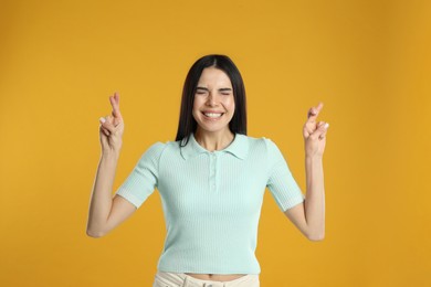 Woman with crossed fingers on yellow background. Superstition concept